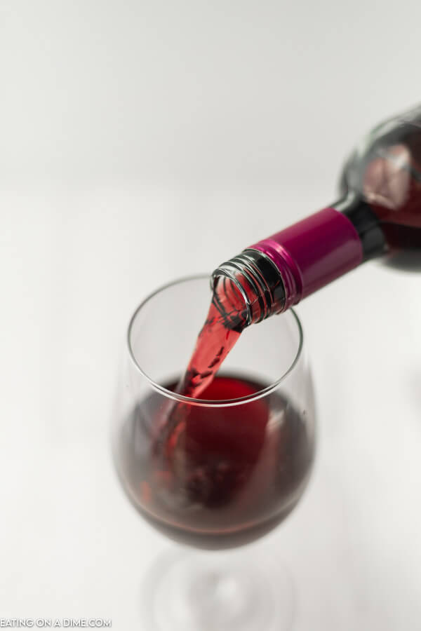 A bottle of red wine being poured into a glass. 