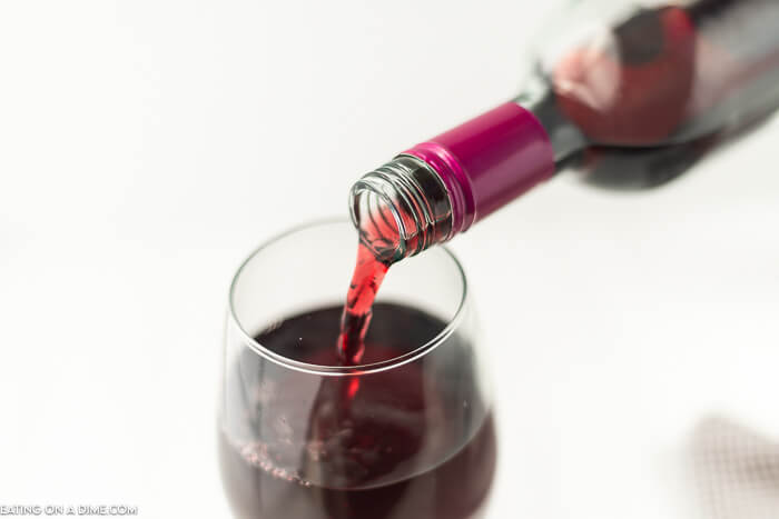 A bottle of red wine being poured into a glass. 