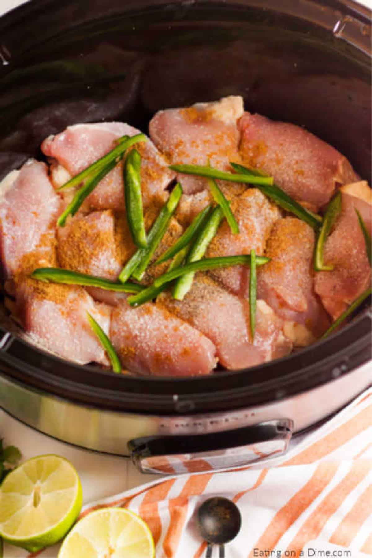 Close up image of uncooked chicken in the crock pot topped with slice jalapenos. 