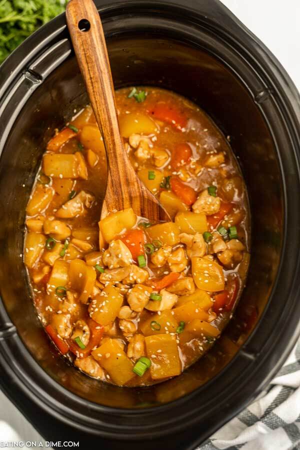 Hawaiian chicken in a crock pot with a wooden spoon. 