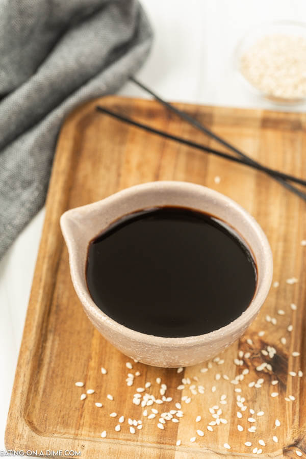 A white bowl of soy sauce on a cutting board