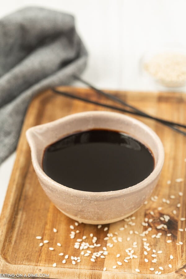 A white bowl of soy sauce on a cutting board