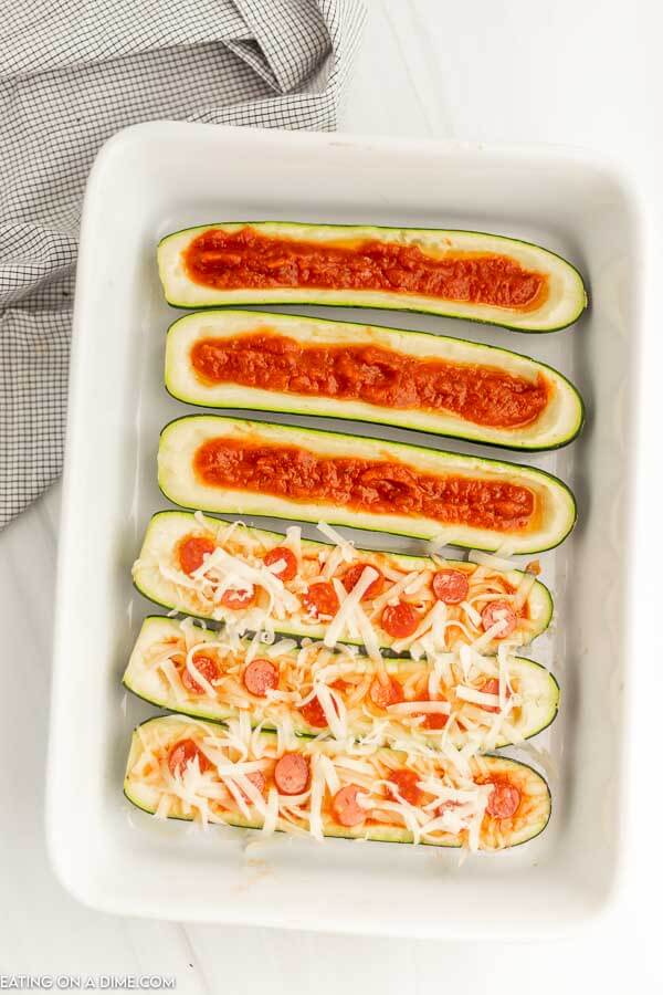 Close up image of making the zucchini pizza boats and topping with pizza sauce and cheese and pepperonis. 