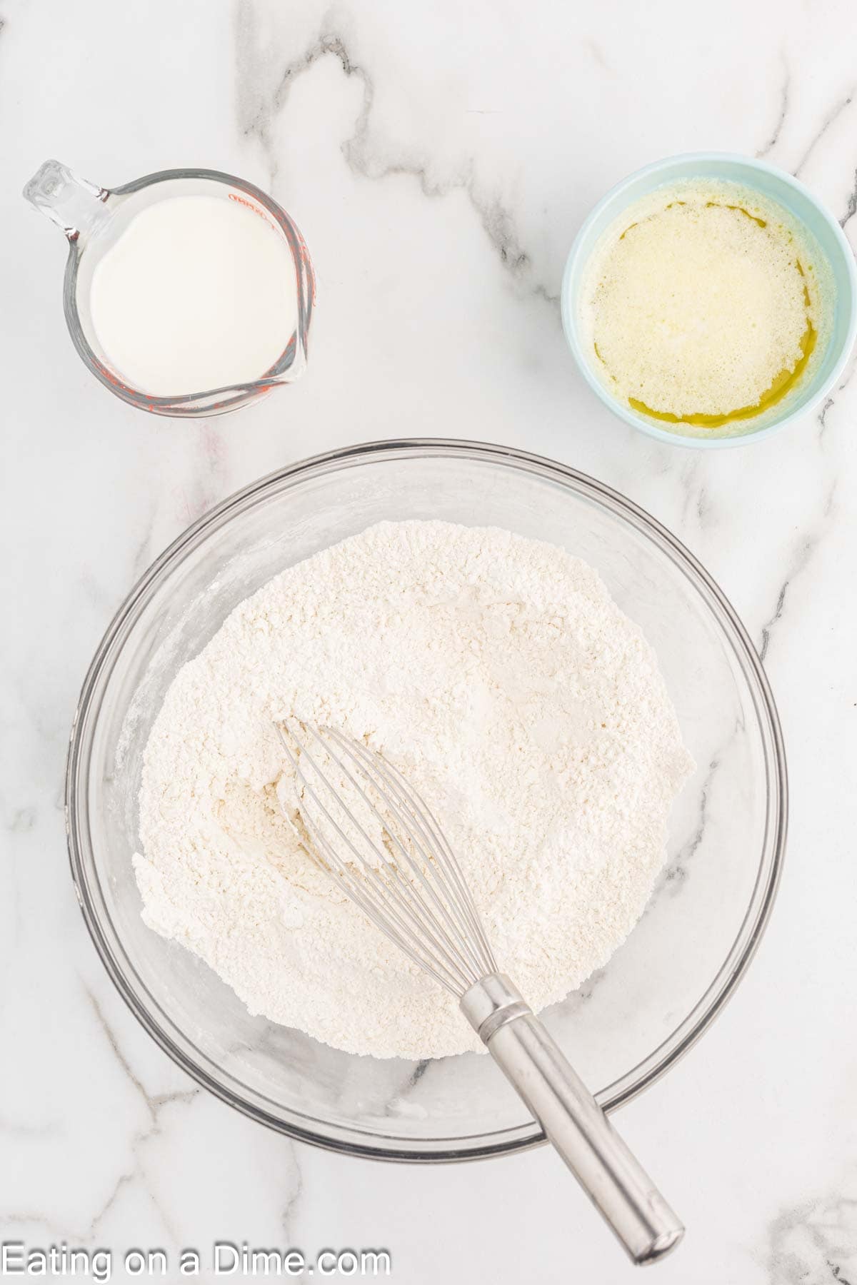Whisking dry ingredients together in a bowl with a small bowl of melted butter and milk on the side