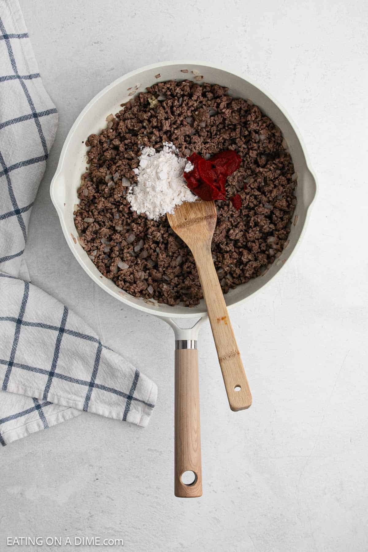 Cooked ground beef topped with flour and tomato paste in a large skillet.
