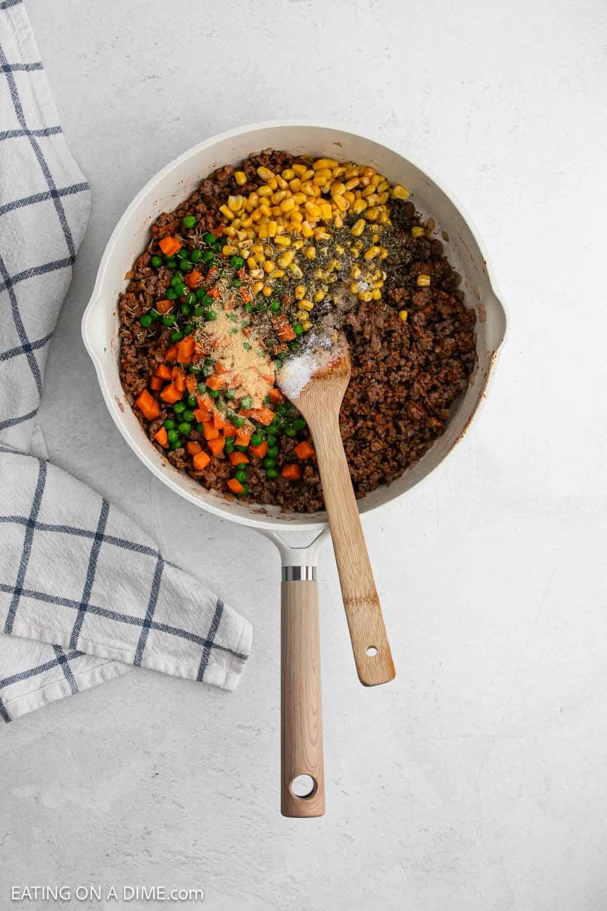 Cooked ground beef in a large skillet topped with spices, corn, and vegetables.