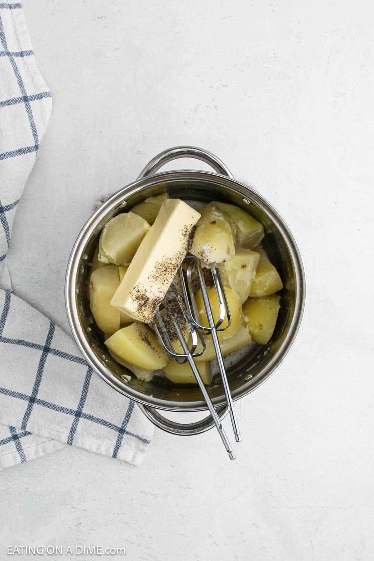 Cooked cut potatoes in a large pot with a stick of butter and spices.