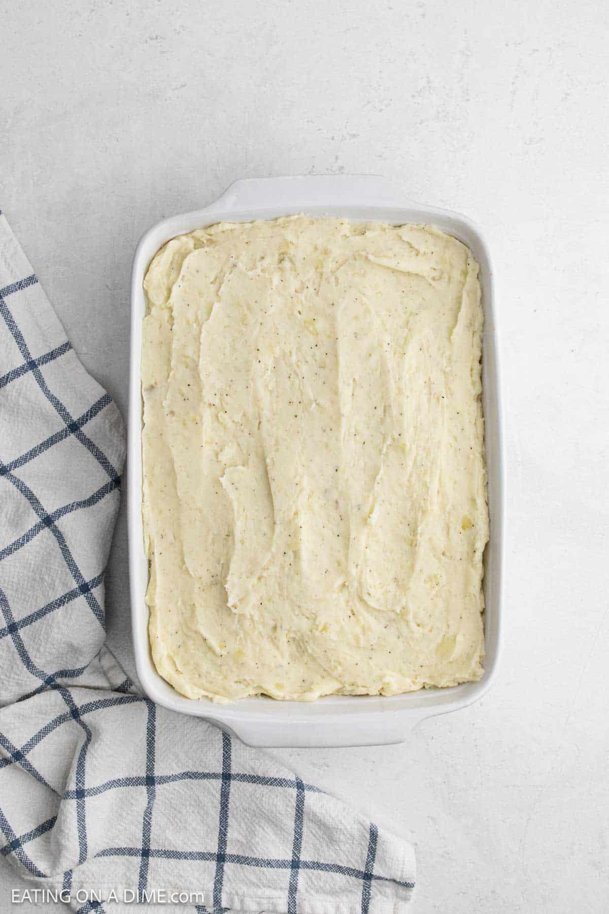 Mashed potatoes spread over the meat mixture in a baking dish.