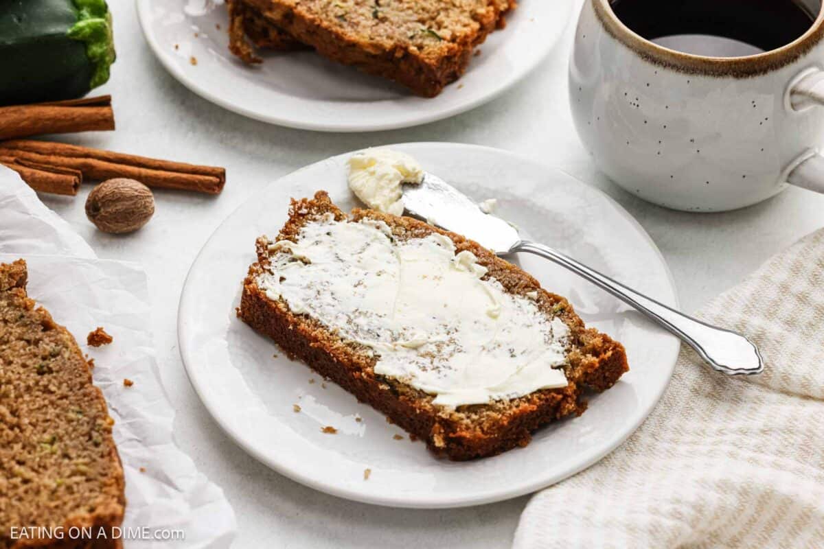 A slice of zucchini bread topped with butter on a plate.