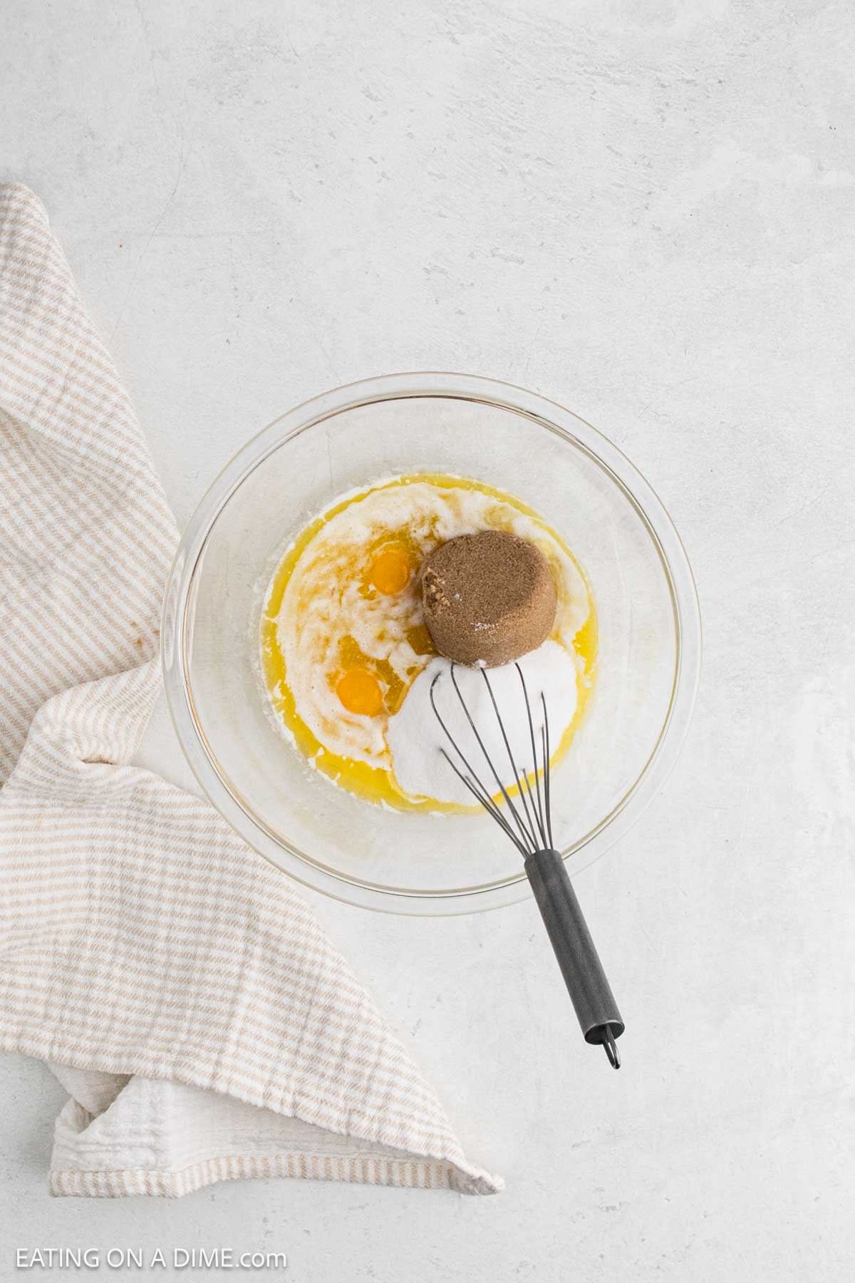 Whisking together eggs, butters, sugars and vanilla in a bowl.