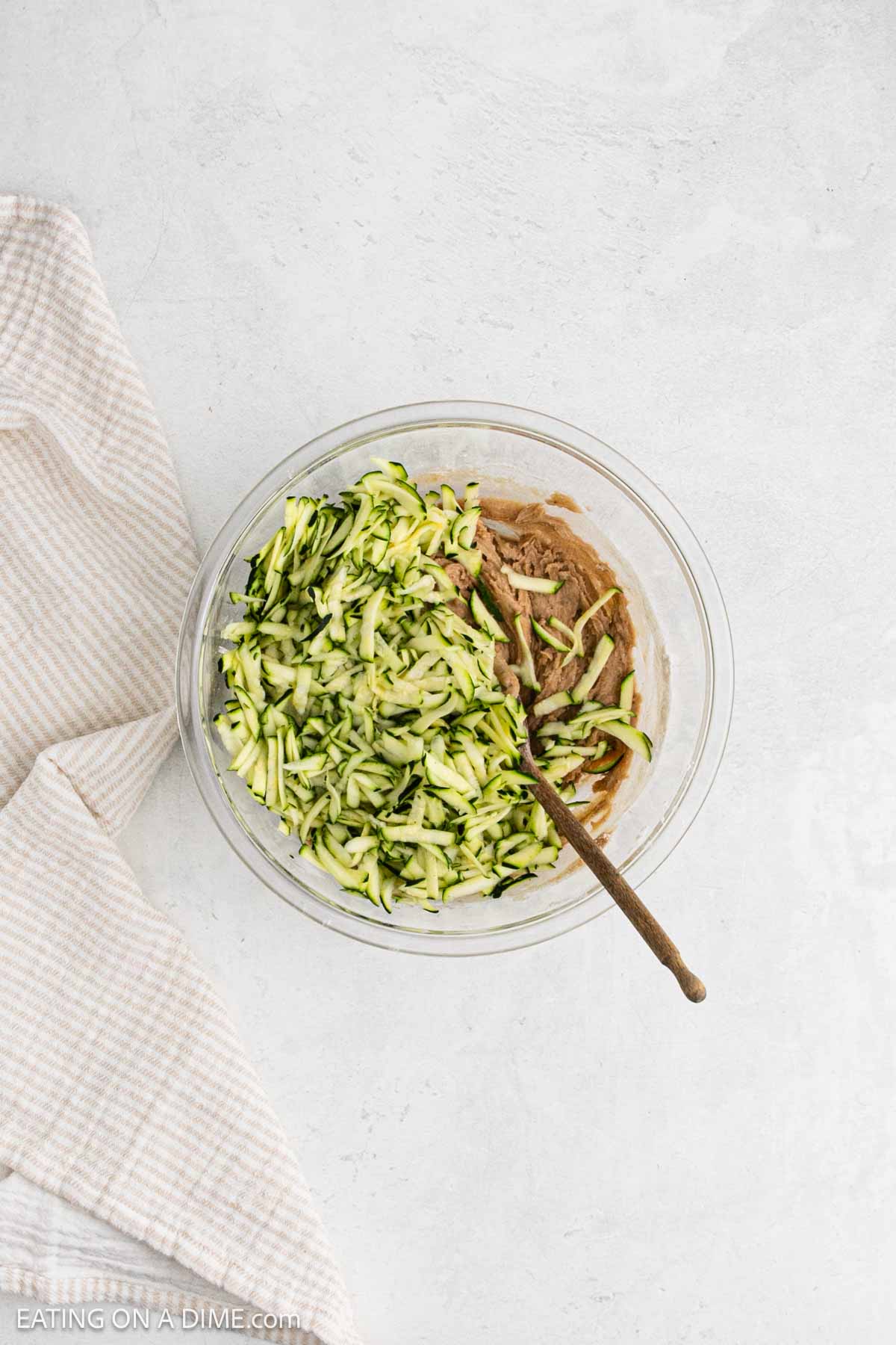 Mixing in the shredded zucchini with the flour mixture in a bowl.