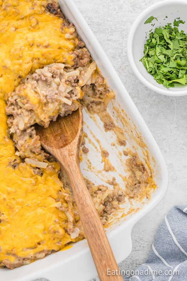 Close up image of hamburger casserole in a baking dish with a wooden spoon.