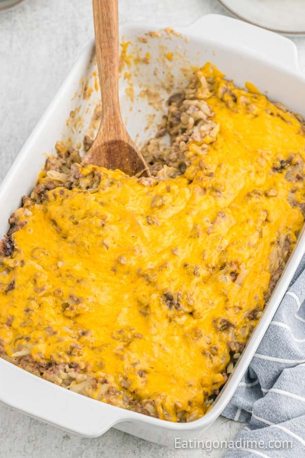 Close up image of hamburger casserole in a baking dish with a wooden spoon. 