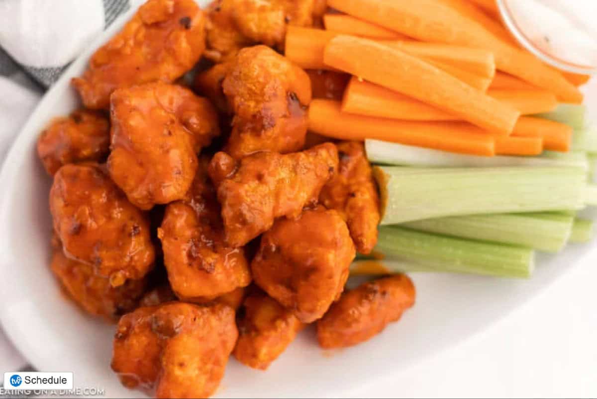 A plate of buffalo cauliflower bites sits alongside crisp celery and carrot sticks, with a cup of dipping sauce in the corner—perfect for pairing with Air Fryer Boneless Chicken Wings at your next gathering.
