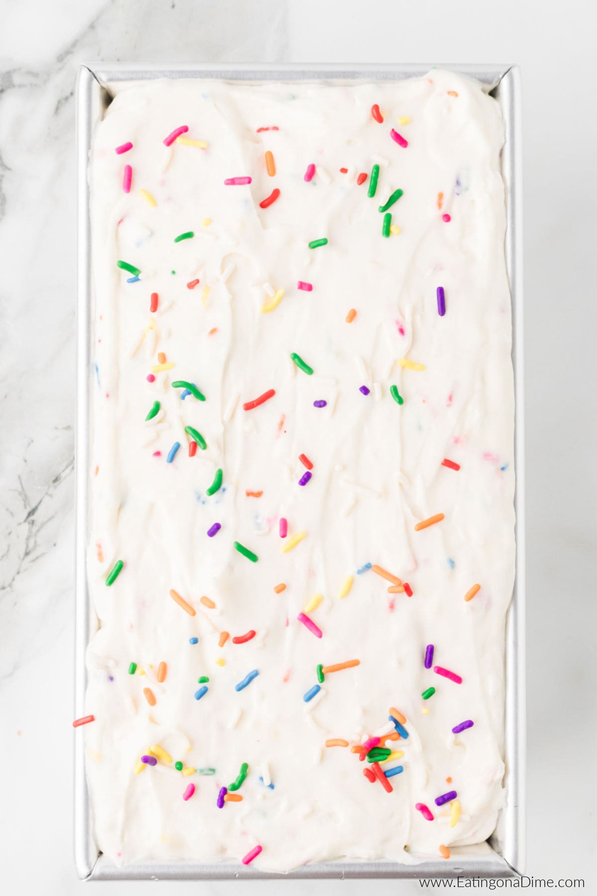Ice cream mixture spread in a loaf pan topped with sprinkles.