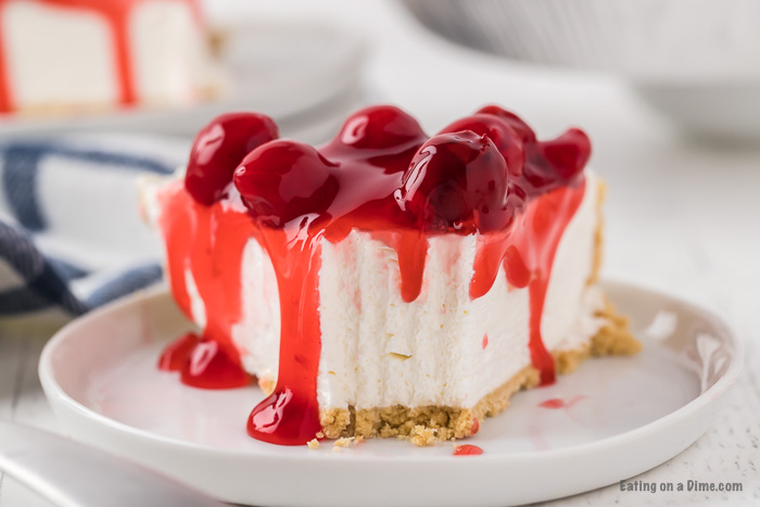 Close up image of a slice of cheesecake on a white plate with cherries on top
