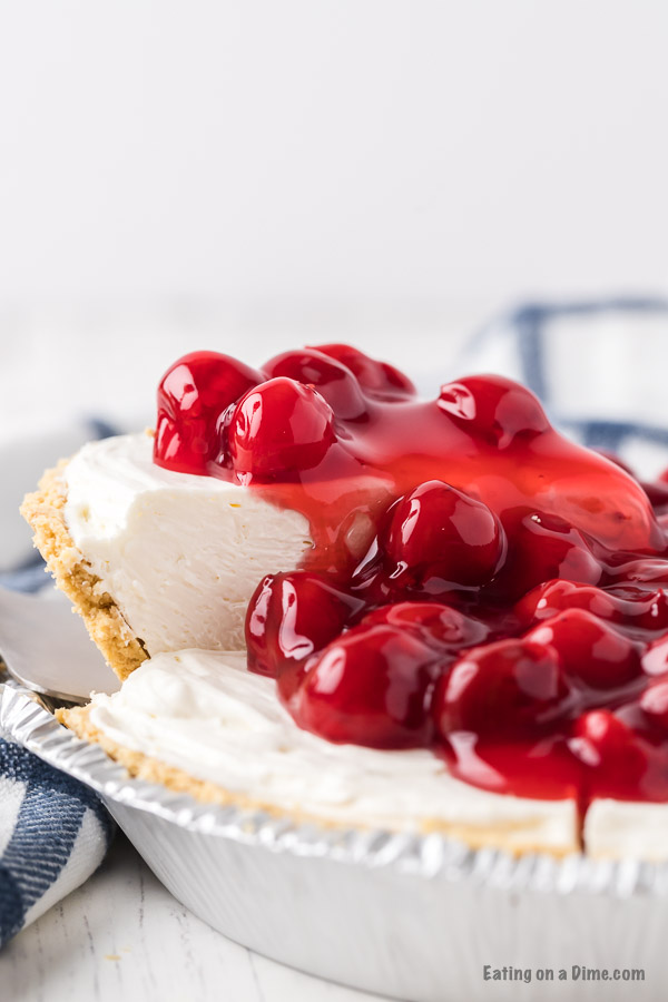 Close up image of a whole cheesecake topped with cherries with a slice being served. 