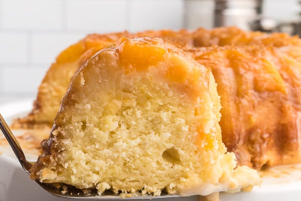 A whole peach cobber pound cake with a slice on a spatula