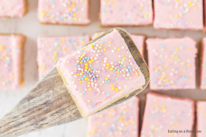 Close up image of sugar cookie bars frosted and a serving on a spatula