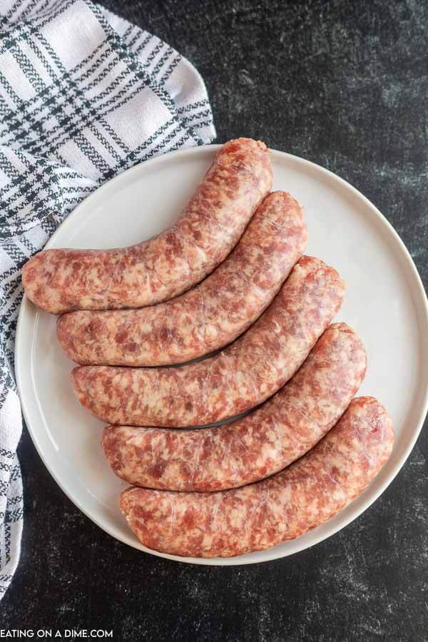 Uncooked  brats on a plate. 