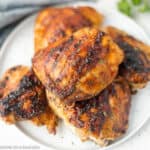 A plate of grilled BBQ chicken thighs, perfectly seasoned with charred grill marks, garnished with fresh herbs.