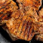 Close-up of Bone In Pork Chops on the Grill with visible sear marks, seasoned with herbs and spices, and garnished with chopped parsley on top.