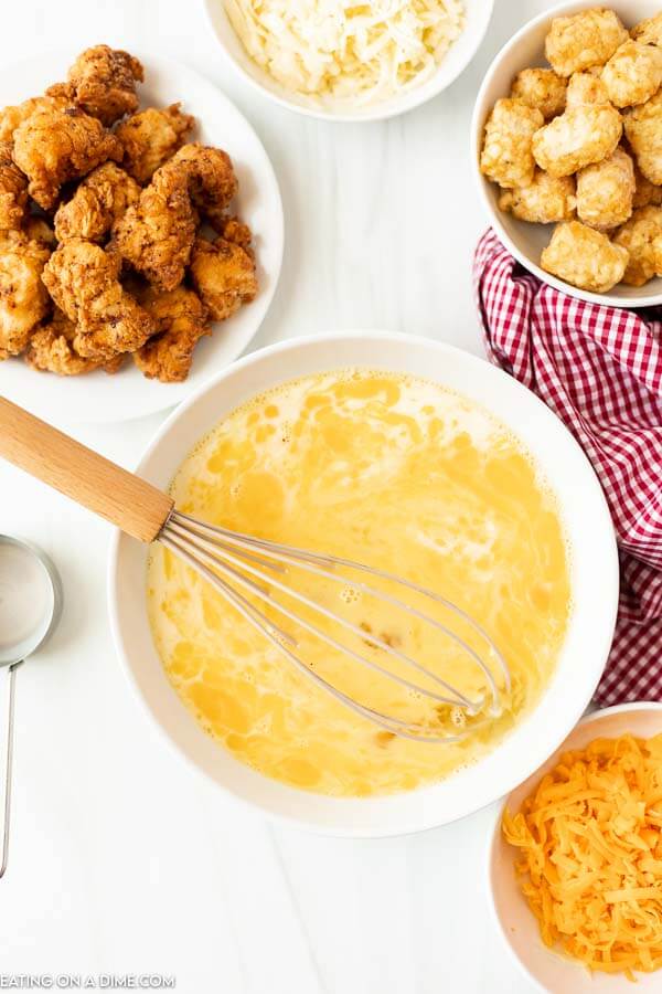 Preparing the eggs in a bowl with a bowl of chicken nuggets and a bowl of cheese and tator tots