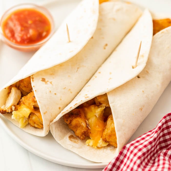 Two breakfast burritos on a white plate with a side of salsa