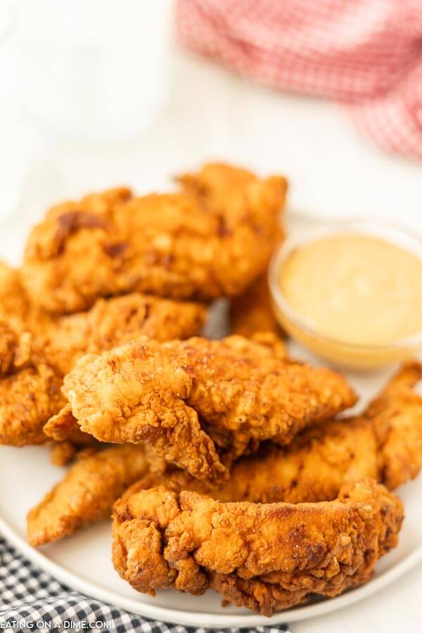 Close up image of chicken tenders on a white plate with dipping sauce