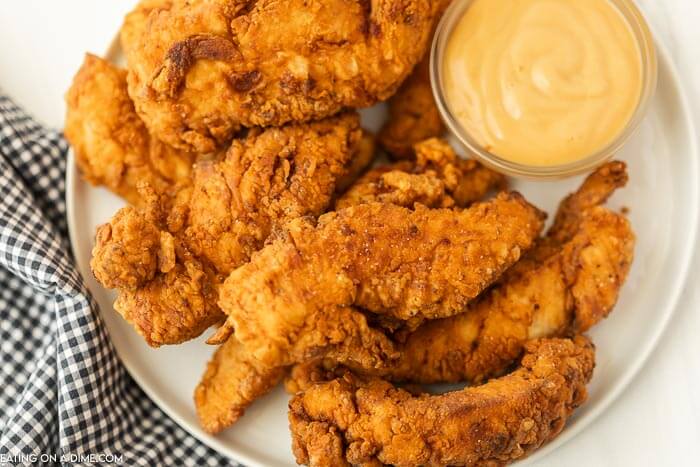 Close up image of chicken tenders on a white plate with dipping sauce