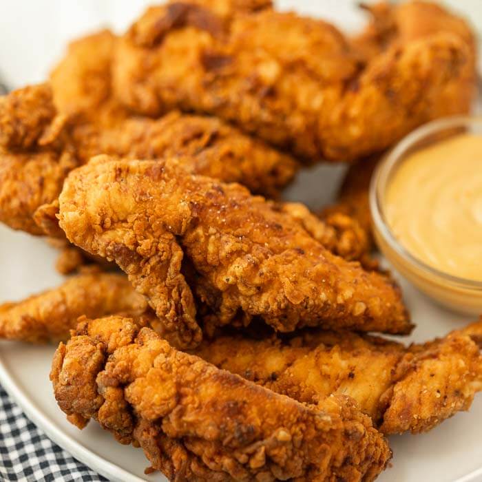 Close up image of chicken tenders on a white plate with dipping sauce