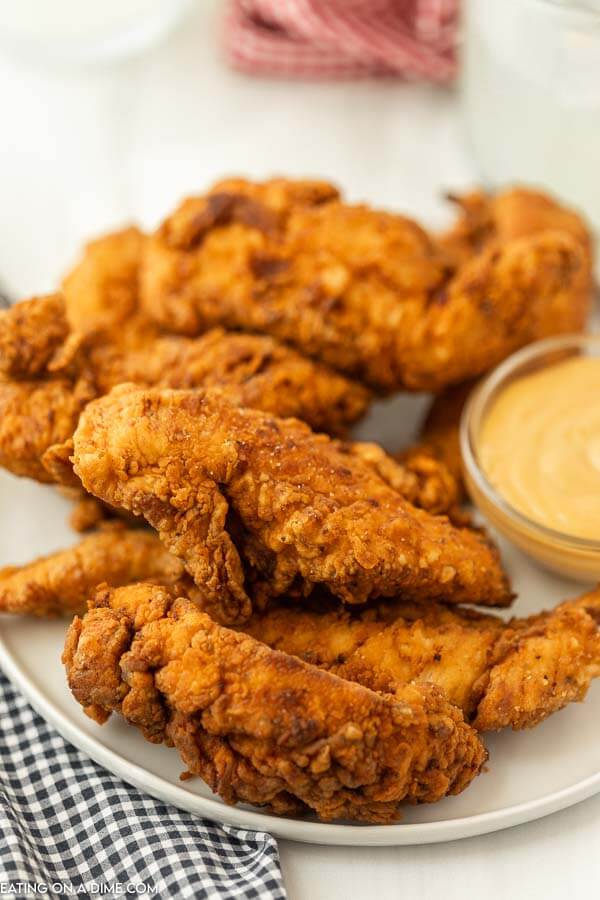 Close up image of chicken tenders on a white plate with dipping sauce