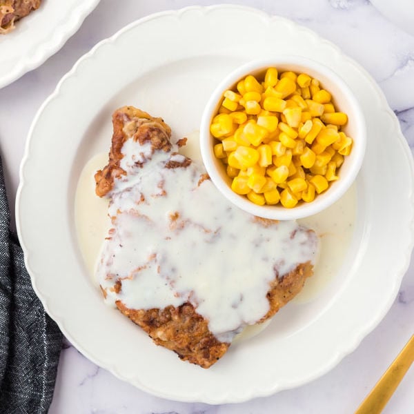 Chicken Fried steak on a white plate with a side of corn
