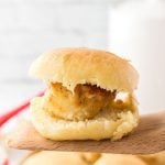 A close-up of a chicken slider with a bite taken out, sitting on a wooden spatula. Reminiscent of Chick-fil-a Chick-n-minis, the sandwich features crispy fried chicken inside a soft, golden-brown bun.