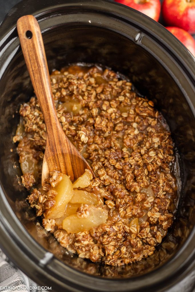 Apple Crisp in the Crock Pot with a wooden spoon
