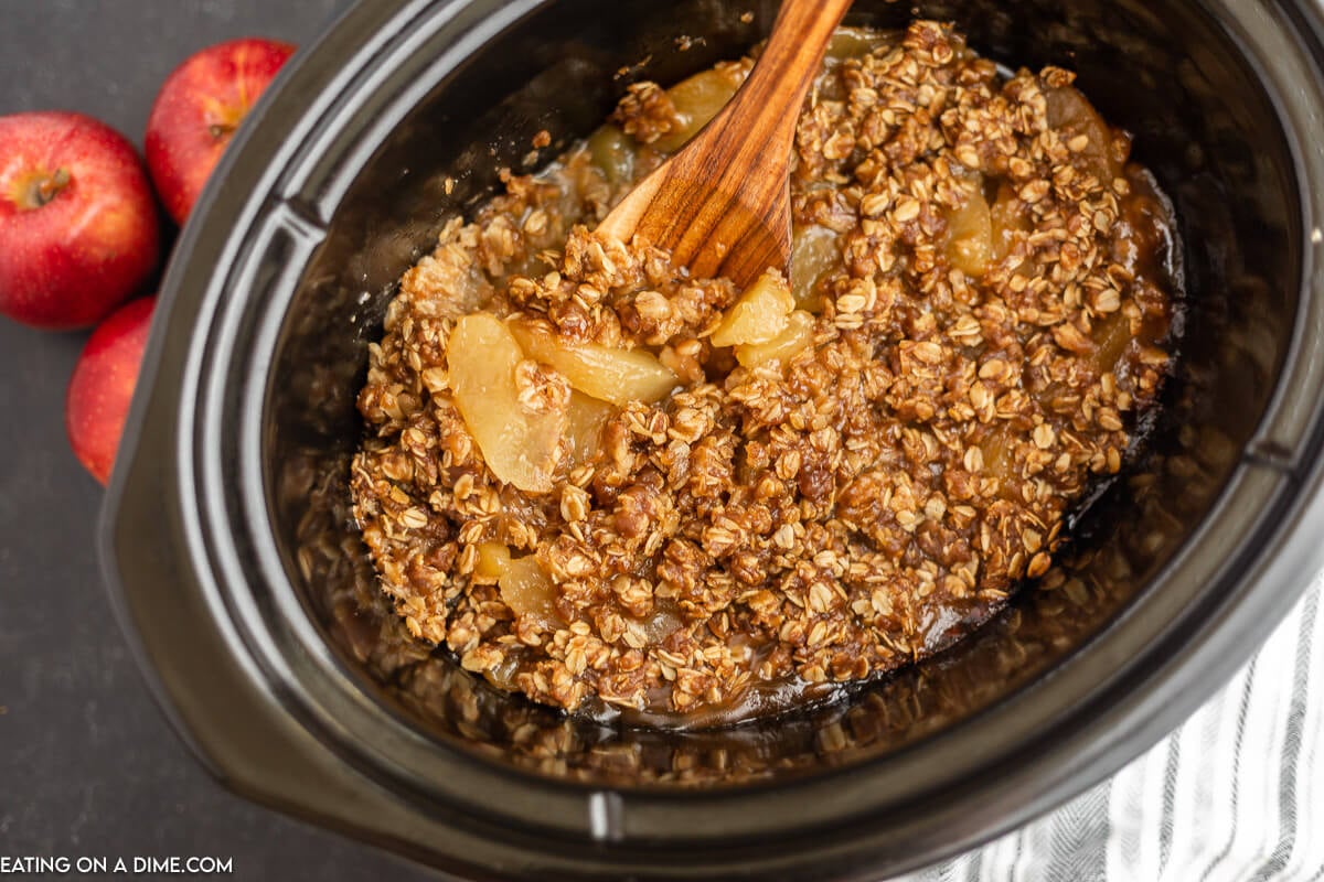 Apple Crisp in the Crock Pot with a wooden spoon