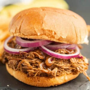 A close-up of a pulled pork sandwich on a bun, topped with sliced red onions. The shredded pork looks moist and saucy—perfect inspiration for your next Crock Pot Brisket Sandwich Recipe.