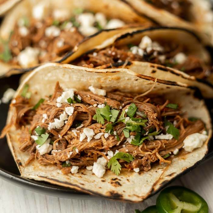 Close up image of shredded beef tacos on a plate.