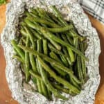Green beans in foil on a cutting board.