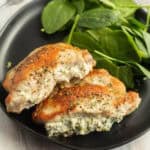 Grilled chicken breast stuffed with creamy filling, garnished with herbs, served on a black plate with fresh spinach leaves, reminiscent of the rich flavor found in baked stuffed pork chops.