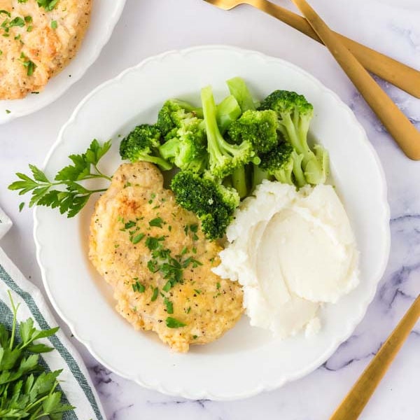 Close up image of fried pork chops on a plate with a side of steamed broccoli and mashed potatoes