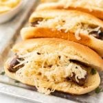 Three hot dogs with sauerkraut on a tray.