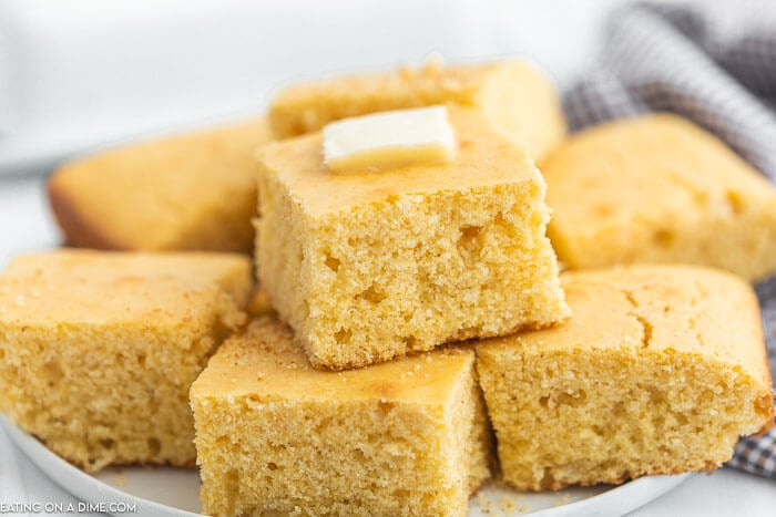 Cut Cornbread stacked on a plate with melted butter on top. 