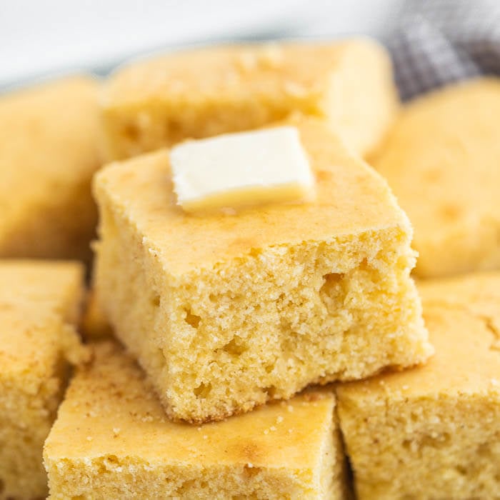 Cut Cornbread stacked on a plate with melted butter on top. 