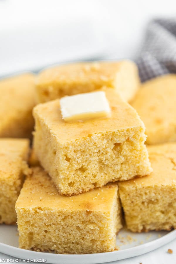 Cut Cornbread stacked on a plate with melted butter on top. 