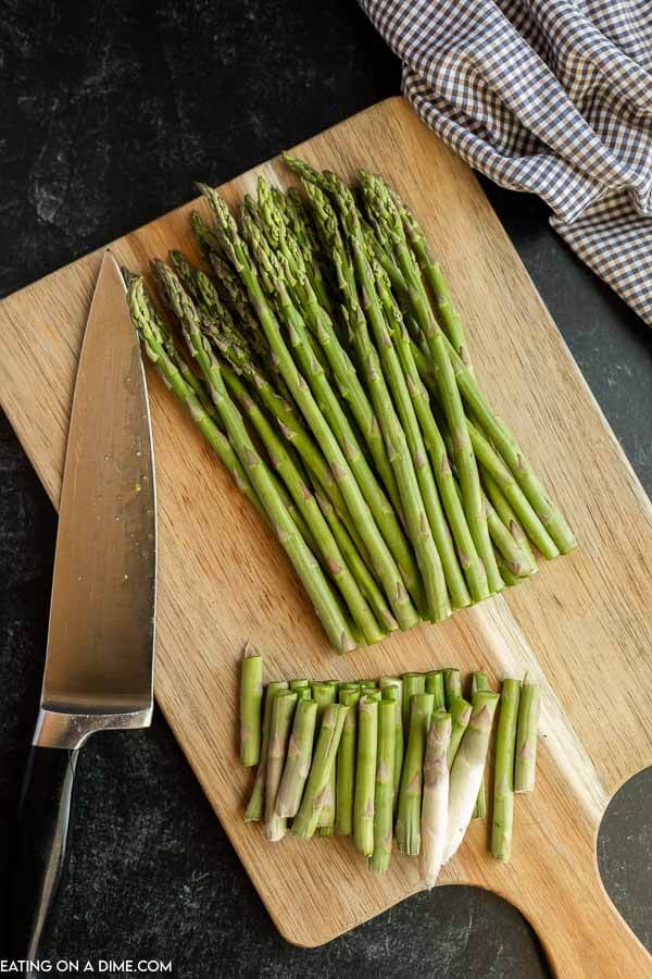 Cutting board with cut asparagus on it with a sharp knife