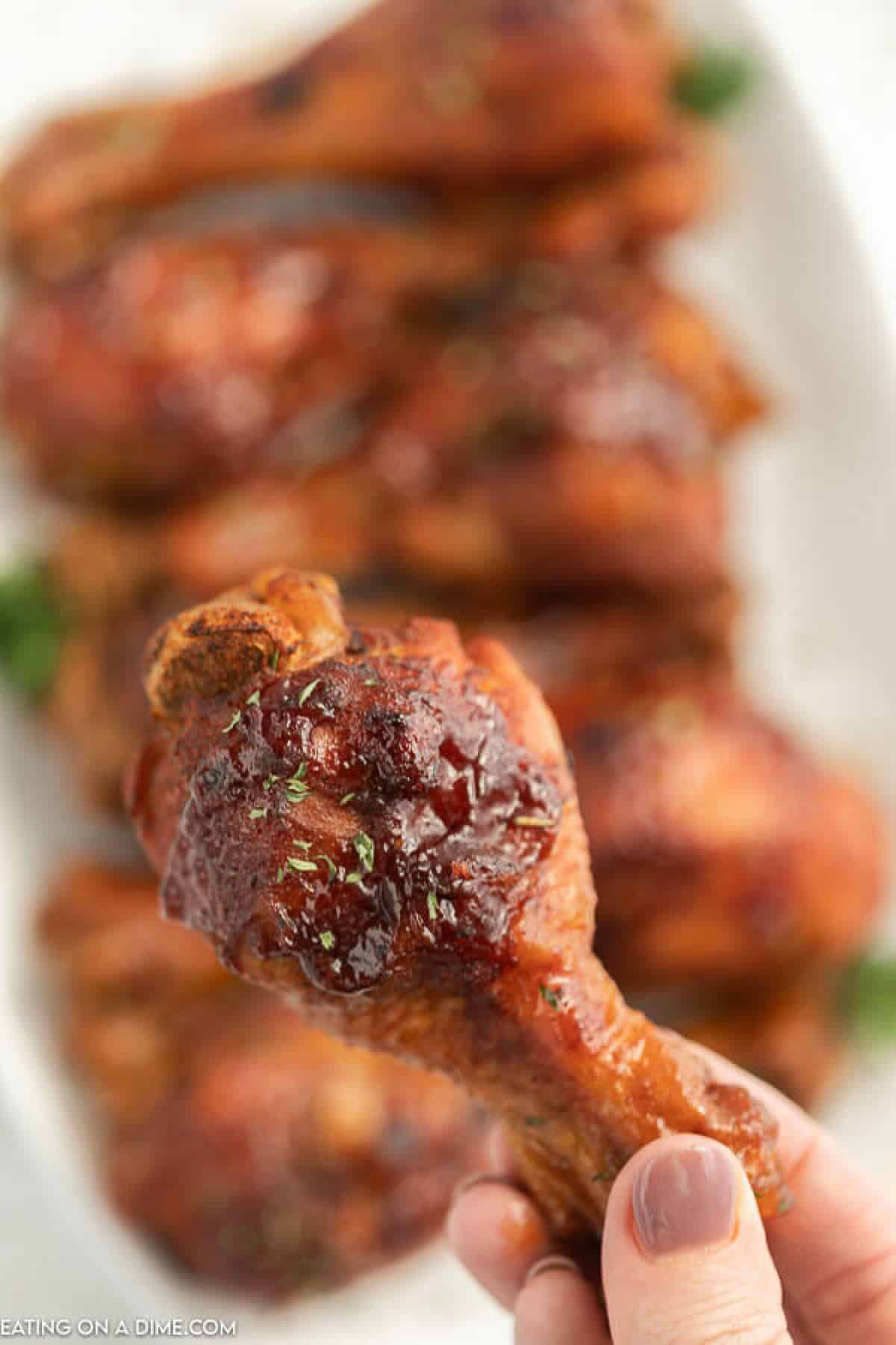 Get dinner on the table fast with easy Instant Pot BBQ Chicken Drumsticks recipe. With just a few ingredients, your family can enjoy drumsticks in minutes. Close up of a cooked Chicken Drumsticks with a white platter full of chicken legs in the back ground