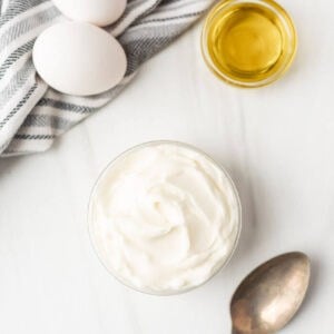 A bowl of mayonnaise near whole eggs and oil.