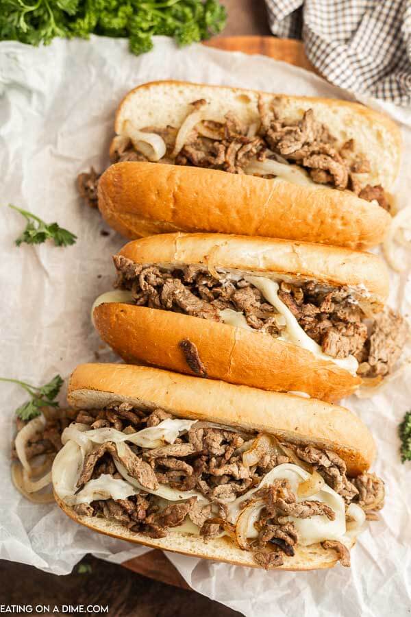 Philly Cheesesteaks lined up on a sheet of wax paper. 