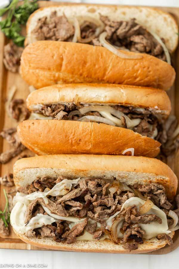 Philly Cheesesteaks lined up on a cutting board. 